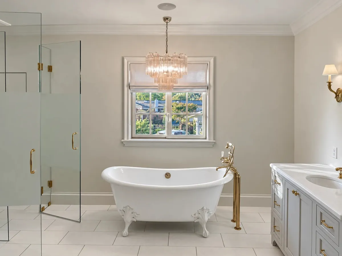 Freestanding clawfoot tub under a window with a crystal chandelier