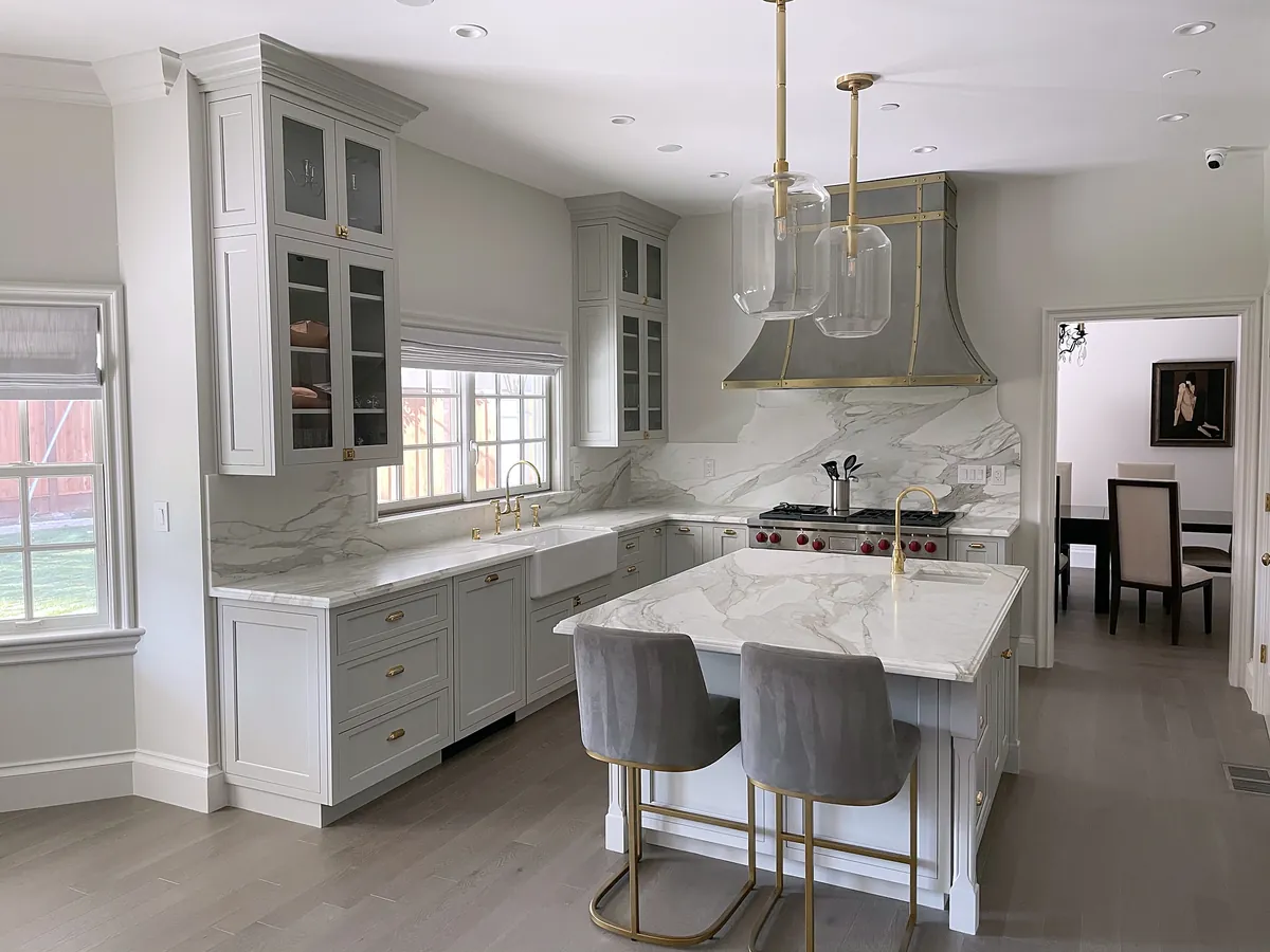Marble kitchen island with gray upholstered stools and pendant lights